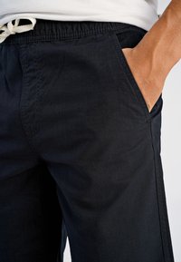 Czarne szorty wykonane z lekkiego materiału, wyposażone w elastyczną talię ze sznurkiem, boczne kieszenie oraz gładką fakturę.