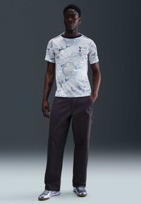 Camisa de manga corta de color azul claro con un patrón veteado y acentos en azul marino, combinada con pantalones gris oscuro y zapatillas plateadas.
