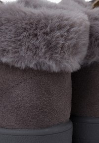 Botas de tobillo de ante gris con un suave puño de piel gris, puntera redonda y suela de goma negra, que presentan detalles de costura en la parte superior.