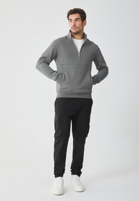 Pulover gri din fleece cu guler cu jumătate de fermoar, având un design simplu, asortat cu pantaloni cargo negri și adidași albi.