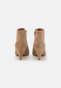 Taupe ruskinds ankelstøvler med en slank hæl og lynlås i siden. Glat tekstur, rund tå og design i midtkalvshøjde.