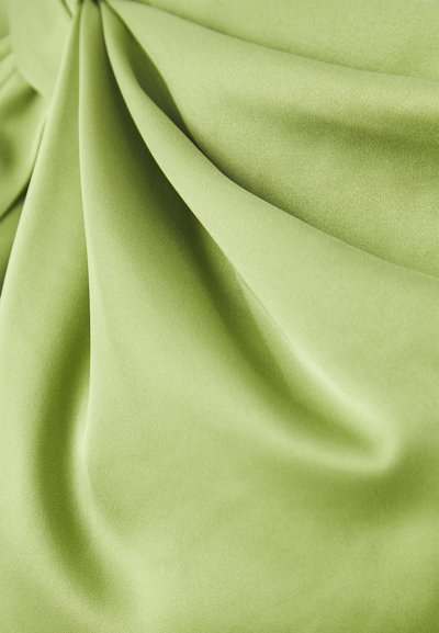 Tessuto verde chiaro con una trama liscia, caratterizzato da morbide pieghe e drappeggi leggeri. La superficie appare leggermente lucida e uniforme.