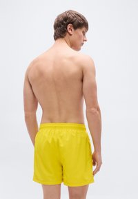 Κίτρινο μαγιό σορτς από ελαφρύ υλικό, με ελαστική μέση και πλαϊνές τσέπες, εμφανιζόμενο από την πίσω όψη.
