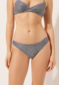 Bikini-set i ett strukturerat svartvitt mönster. Toppen har en vriden design och trosorna har en låg midja med minimal täckning.