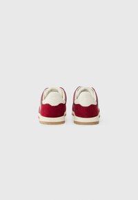 Røde ruskinds sneakers med hvide accenter, rundede former, en tekstureret overflade og en lille hæl. Bemærkelsesværdigt scallopdesignet bagpå.