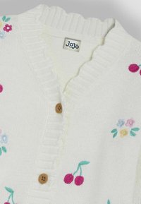Cárdigan blanco de punto con un escote en forma de ondas, botones de madera y bordados florales en rosa, azul, amarillo y verde.