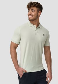 Hellgrünes Poloshirt mit kurzen Ärmeln, aus strukturiertem Stoff. Verfügt über einen Kragen und ein kleines gesticktes Logo auf der linken Brust.