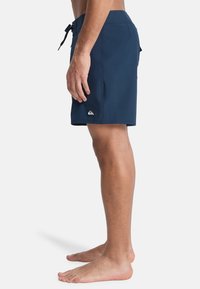 Ναυτικό μπλε μαγιό φτιαγμένο από ελαφρύ υλικό, με κλείσιμο κορδονιού, πλευρικές τσέπες και λογότυπο κοντά στο στρίφωμα.