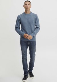 Lys blå strikket genser med rund hals, ribbede mansjetter, parret med mørkeblå jeans og svarte joggesko. Enkelt design, ingen synlige mønstre.