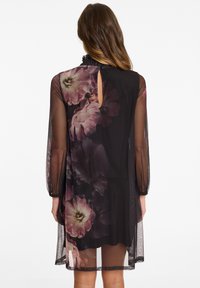 Transparante zwarte jurk met een bloemenprint in roze en paarse tinten, met lange mouwen en een keyhole-detail op de achterkant.