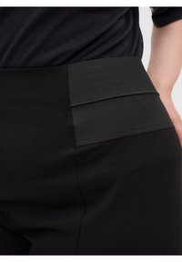 Leggings noirs à la texture lisse, avec une large ceinture élastique et des détails de panneaux contrastants de la même couleur.