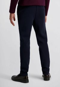 Marineblauwe broek met een rechte snit, gladde textuur, achterzakken en een nette afwerking. Combinatie met donkere schoenen, gezien vanaf de achterkant.