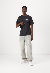 Black cotton t-shirt with a small graphic on the chest, paired with light blue denim jeans featuring contrasting stitching and a relaxed fit.