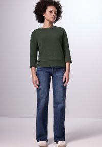 Mörkgrön, strukturerad tröja med trekvartslånga ärmar i kombination med blå, raka jeans och ljusa skor. Enkel, avslappnad look.
