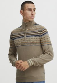Beige cipzáras nyakú pulóver, amely texturált mintával rendelkezik, kék, barna és krém színű akcentusokkal, bordás mandzsettákkal és laza szabással.