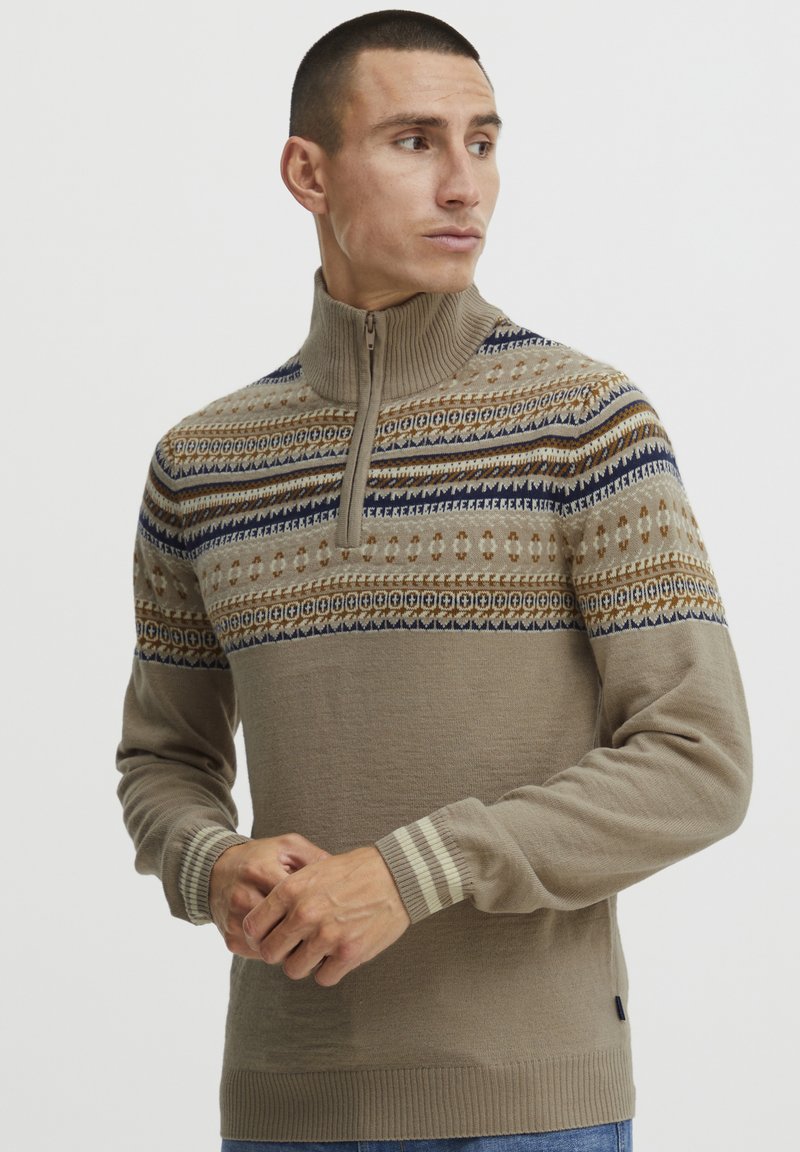 Beige cipzáras nyakú pulóver, amely texturált mintával rendelkezik, kék, barna és krém színű akcentusokkal, bordás mandzsettákkal és laza szabással.