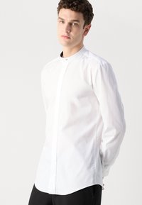 Camisa blanca de manga larga con cuello mao, con un cierre frontal discreto y tela suave y ligera. Diseño simplistic.