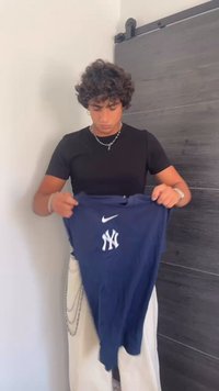 Plavi dugosleeve majica s bijelim logotipom New York Yankees i Nike brendiranjem, drži osoba koja nosi crnu majicu i svijetle hlače.