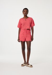 Roze oogjes kant top met opgezette mouwen, gecombineerd met bijpassende shorts met een gestrikt middel. Draag met lichte sandalen.