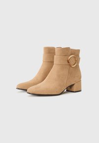 Bottes de cheville en daim tan avec un bout pointu, un talon épais et une large sangle dotée d'une boucle ronde en or.