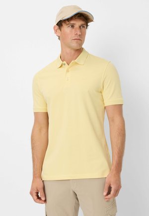 Polohemd aus weichem gelbem Baumwollstoff mit klassischem Kragen, zwei Knöpfen und kurzen Ärmeln. Ergänzt durch eine beigefarbene Kappe mit blauen Akzenten.