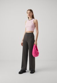 Svetloružový crop top s detailom písmen, tmavé rebrované nohavice s širokými nohavicami a jasne ružová chlpatá taška. Celkový look dotvárajú hrubé čierne topánky.