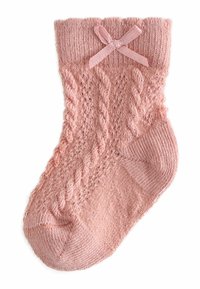 Šviesiai rožinė megzta kojinė su tekstūruotu pynimo raštu ir dekoratyvine kaspino detale ant viršaus, lygiu pirštu ir raištu viršutine dalimi.