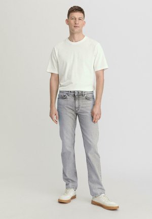 White cotton t-shirt, gray straight-leg jeans, and white sneakers with a textured sole. Model stands against a plain background.