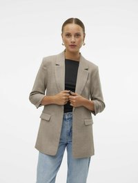 Lys brun blazer med teksturert stoff, en-knapp design, notched lapels og påsydde lommer, brukt over en svart topp og blå jeans.