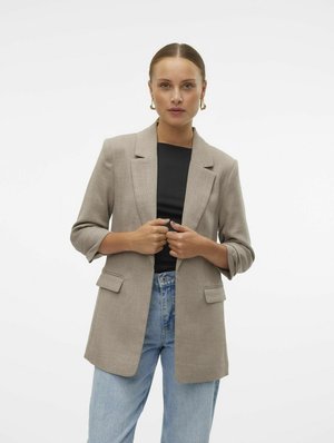 Light brown blazer with a textured fabric, single-breasted design, notched lapels, and patch pockets, worn over a black top and blue jeans.