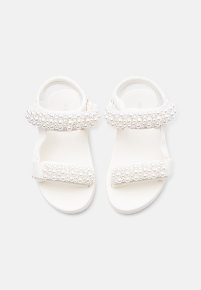 Λευκά σανδάλια με δύο λουράκια διακοσμημένα με σειρές μικρών λευκών μαργαριταριών, σχεδιασμένα με ανοιχτή μύτη και λουράκι στον αστράγαλο.