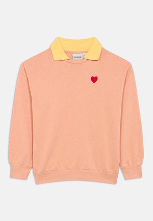 Ružový dlhý rukáv mikina so žltým golierom a malým červeným srdcom na hrudi, zložená na bielo pozadí.