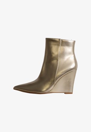 Bottine dorée brillante avec bout pointu et talon compensé, finition cuir lisse, détail de couture latérale et semelle basse.