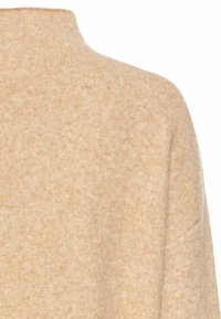 Beige strikket sweater med høj hals, tekstureret stof og blød overflade. Søm detaljer er synlige på skulderen og siden.
