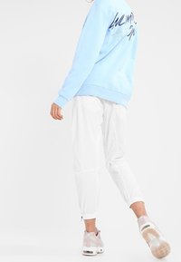 Felpa azzurra con grafica "Unlimited Action" sul retro, abbinata a pantaloni jogger bianchi e sneakers rosa con suola traslucida.
