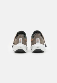 Nike sneakers met een bruin gestructureerd bovenmateriaal, een witte tussenzool en een zwarte buitenzool, met oranje en reflecterende details op de hiel.