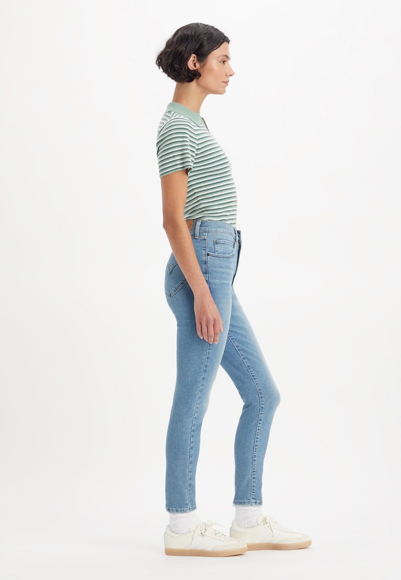 Gestreiftes grünes Kurzarmhemd, hellblaue High-Waist-Jeans und weiße Sneakers mit hellen Sohlen. Einfaches Design, taillierte Silhouette.