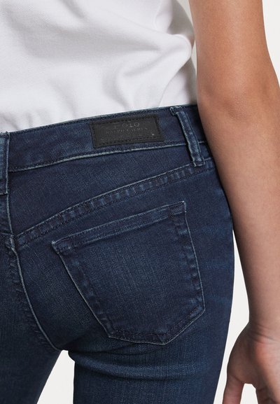 Jeans de mezclilla azul oscuro con corte slim, que cuentan con un bolsillo trasero y un parche de cuero con el logo en la cintura. Diseño limpio, con costuras mínimas.