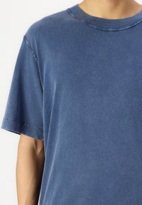T-shirt in cotone blu con una vestibilità comoda, maniche corte e scollo rotondo. Il tessuto ha una texture morbida con una finitura leggermente sbiadita.