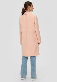 Jasnoróżowy płaszcz z mieszanki wełny z wyraźnym kołnierzem, długimi rękawami i prostym krojem, w połączeniu z jasnoniebieskimi dżinsami w fasonie dzwonów.