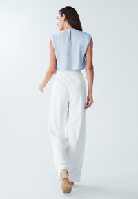 Lyseblå cropped top med detail med nøglehul i ryggen, parret med løse hvide bukser. Outfittet har en tekstureret finish og er accessoriseret med hæle.