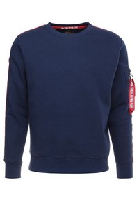 Sudadera azul marino de algodón, con cuello redondo, puños acanalados y un bolsillo con cremallera en la manga izquierda con una etiqueta roja.