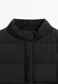 Giacca nera imbottita con colletto alto, caratterizzata da sezioni trapuntate e una consistenza morbida e liscia. Design minimalista senza hardware visibile.