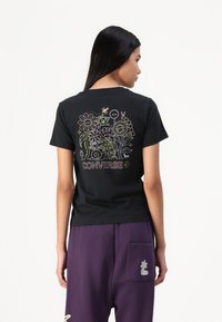 T-shirt preto de manga curta com um design floral colorido e o texto "CONVERSE" num estilo divertido nas costas. Material de algodão suave.