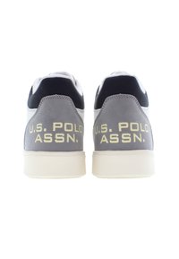 Šedé a bílé tenisky s hladkým koženkovým povrchem. Obsahují černé akcenty a vyražený text "U.S. POLO ASSN." na patě.