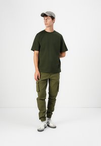 Olive green cotton T-shirt paired with olive cargo pants featuring side pockets and elastic cuffs, complemented by gray cap and white sneakers.