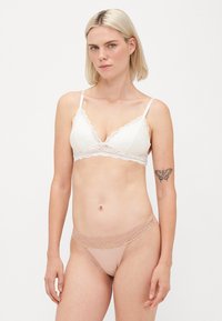Wit bralette met kantafwerking en verstelbare bandjes, gecombineerd met een huidkleurige string met een vergelijkbare kanten tailleband. Glad stoffen afwerking.