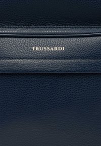 Borsa in pelle testurizzata blu navy con zip liscia e brandizzazione in argento "TRUSSARDI" sul davanti.