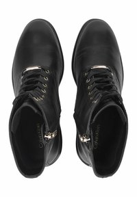 Botas de tobillo de piel negra con textura suave, herrajes en tono dorado, cordones en la parte delantera y detalle de cremallera en el lateral; suelas planas.