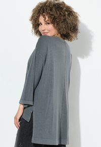Graues übergroßes Oberteil mit 3/4-Ärmeln und seitlichen Schlitzen. Weicher Stoff mit feiner Textur und schlichten Nahtdetails.